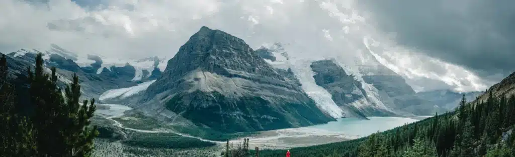 Mt. Robson Heli-Tour "The Majestic Tour" 6 A hiker is perched on a trail. In the background is Berg Lake and Mt Robson.