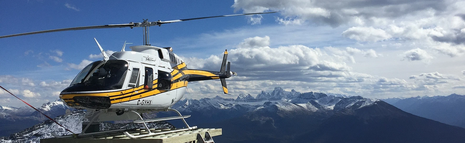 Photo of Yellowhead Helicopters Bell 206 C-GYHX sitting on a heli-pad with the Rocky Mtns in the background