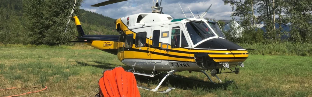 Photo of Bell 212 helicopter landed in field with firefighting Bambi bucket neadby