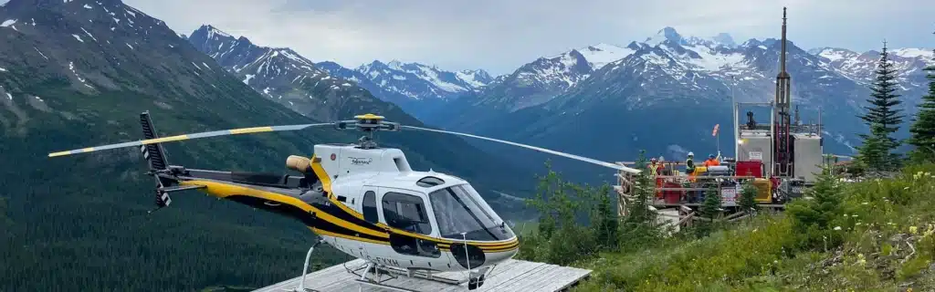 Photo of AS350B3e helicopter landed on a mountain helipad near a mineral exploration drill