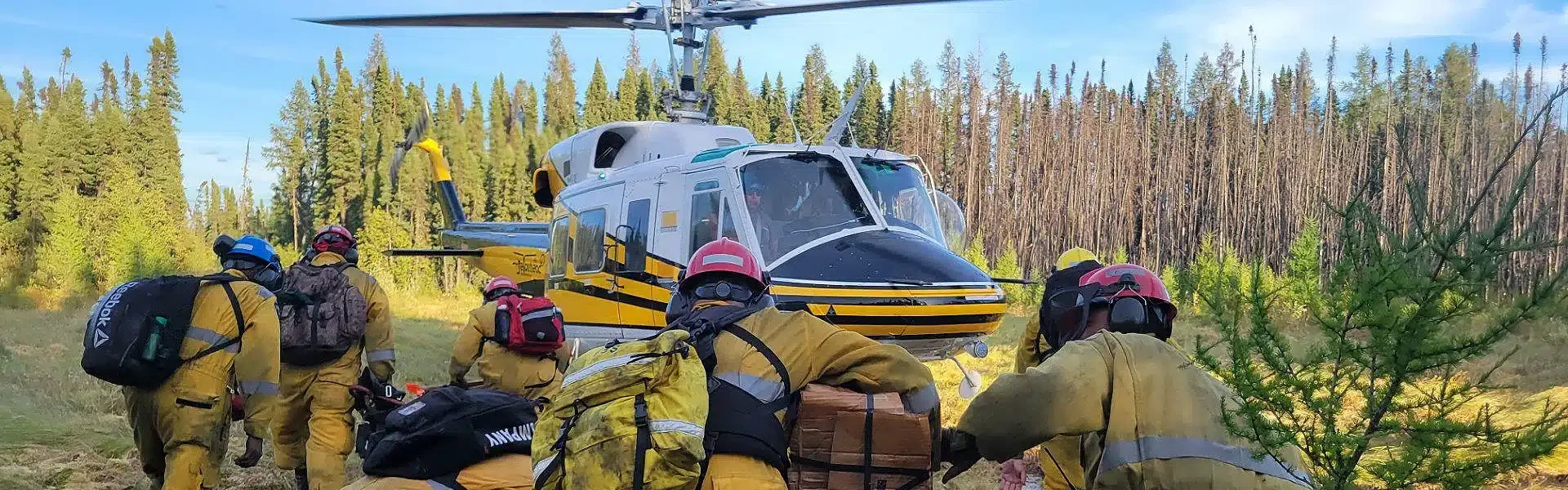 Bell 212 helicopter standing by to load wildfire crew near pine forest